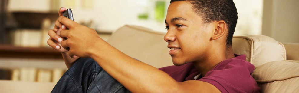 A teenage boy is using the ZAPS College Vocabulary Challenge on his smartphone app while sitting on a couch at home