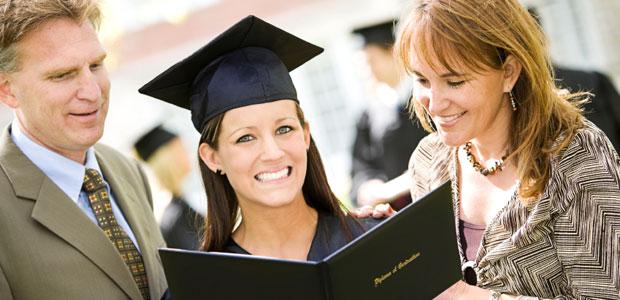 A girl wearing a cap and gown is holding her graduation diploma while her parents look on.